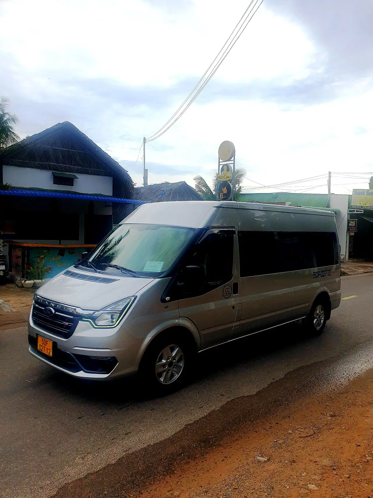 A silver limousine minivan used for passenger transfers, parked on a street in Phan Thiet, Vietnam